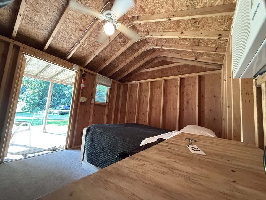 Double bed and ceiling fan inside a rustic cabin, with the door open to the porch